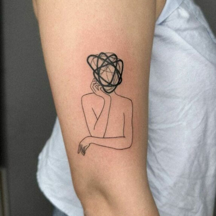 Minimalistic self-love tattoo of a person with a tangled scribble head on an arm, symbolizing deep meaning and empowerment.
