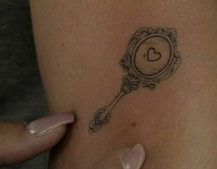 Ornate hand mirror tattoo with heart symbol, symbolizing self-love and personal empowerment.