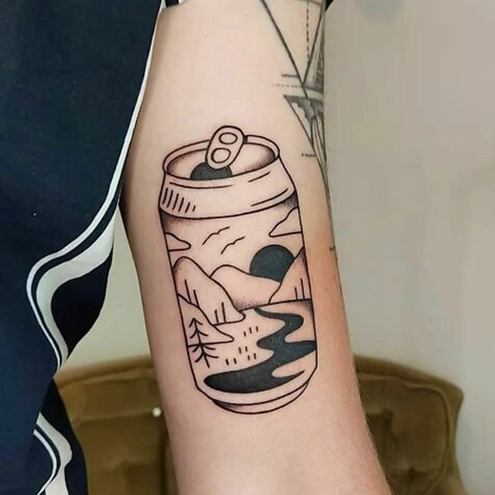 Arm tattoo depicting a soda can with a mountain and river landscape, representing self-love and personal empowerment.