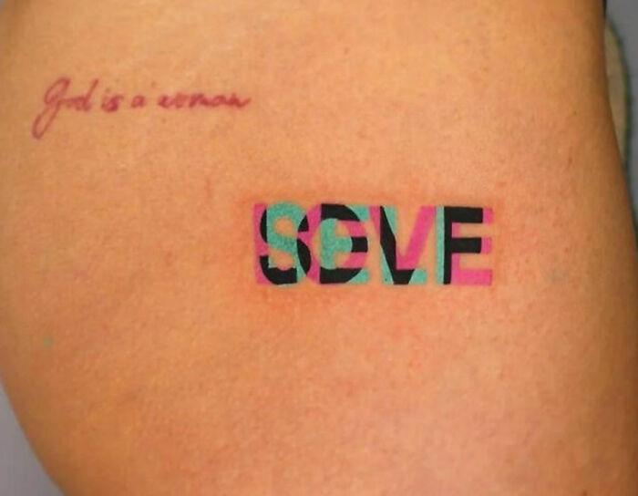 Self-love tattoo with overlapping blue, pink, and black lettering on skin.