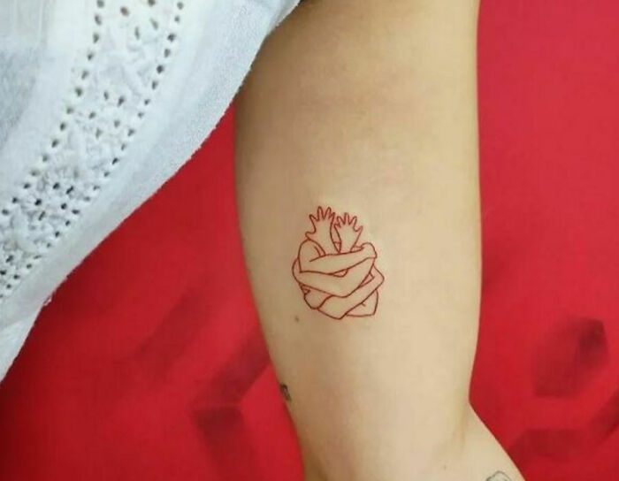 Self-love tattoo of an arm hugging itself on red background.