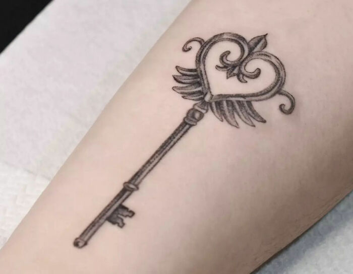 Self-love tattoo featuring a key with a heart design on the forearm.