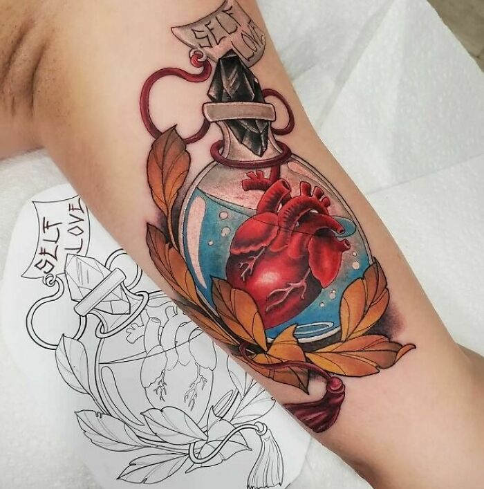 Colorful self-love tattoo featuring an anatomical heart in a bottle, surrounded by autumn leaves on an arm.