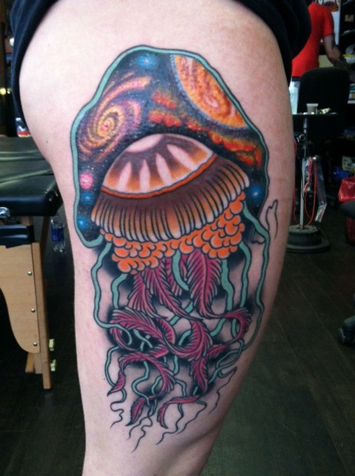 A vibrant space tattoo featuring a cosmic jellyfish design with galaxy elements and colorful details on the thigh.