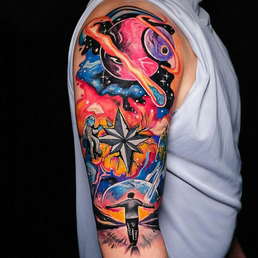 Colorful space tattoo featuring planets, astronauts, and a star compass on an arm showcasing outer space cool.
