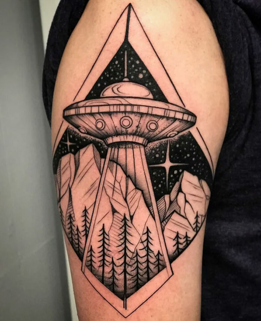 Space tattoo featuring a UFO beaming lights over a forest and mountains, set within geometric shapes.