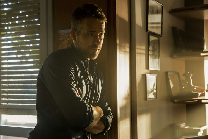 Actor standing thoughtfully in dim light near window blinds, representing one of the highest-paid actors of all time.