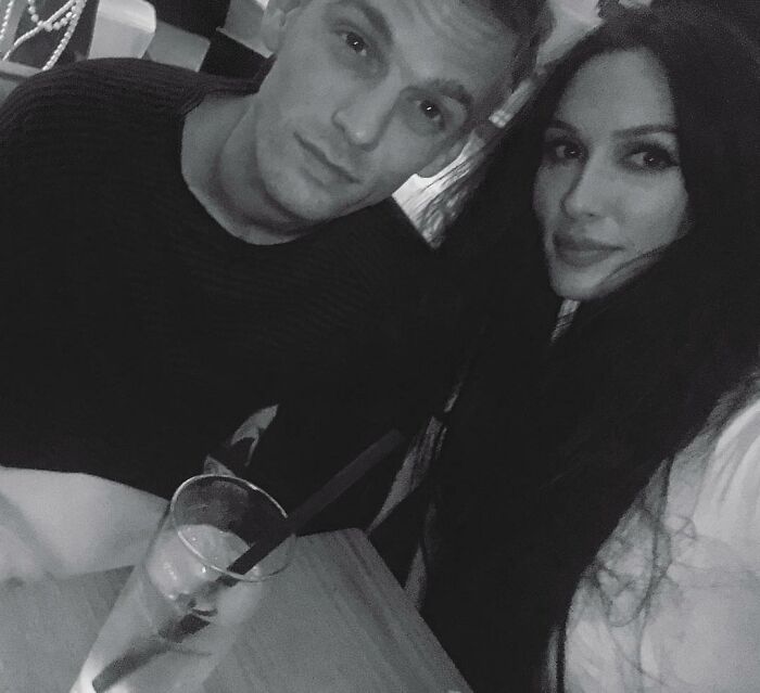 Black and white photo of celebrity twins sitting at a table with a drink, showcasing celebrity twins together.