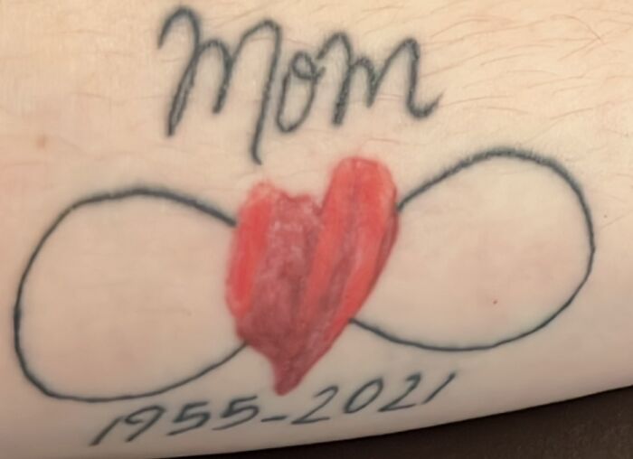 Tattoo of the word "Mom" with an infinity symbol and a red heart, dated 1955-2021.
