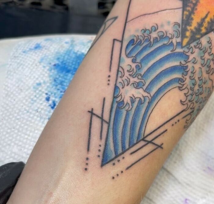 Geometric tattoo on arm featuring a stylized ocean wave with intricate line designs.