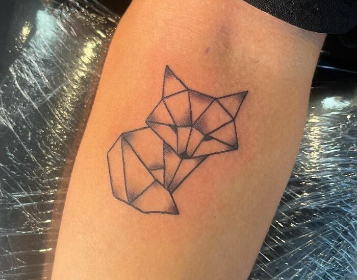 Geometric tattoo of a fox on an arm, featuring angular lines and shapes.