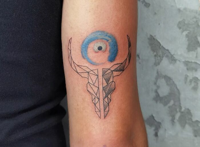 Geometric tattoo featuring abstract bull and blue circle on a person's arm.