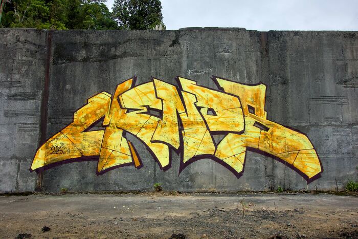 Yellow and orange creative graffiti art painted on a large blank concrete wall outdoors in an urban setting