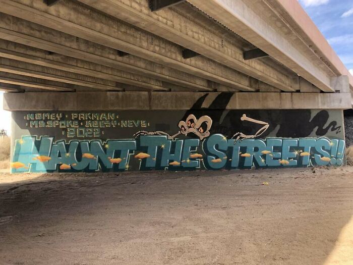 Graffiti art under a bridge depicting a character and the phrase Haunt the Streets in vibrant colors on a blank wall.