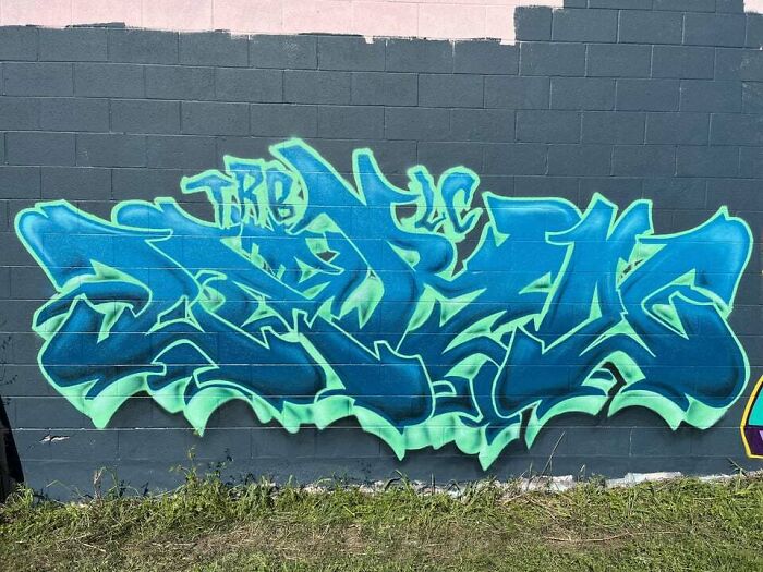 Colorful creative graffiti art in blue and green tones on a gray wall, turning a blank wall into an admired artwork.