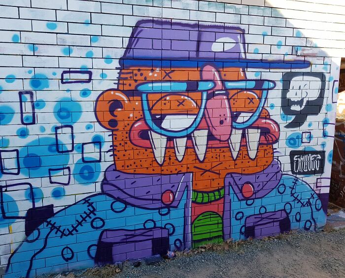 Colorful creative graffiti art on a brick wall depicting a character with glasses and a purple hat in urban style.