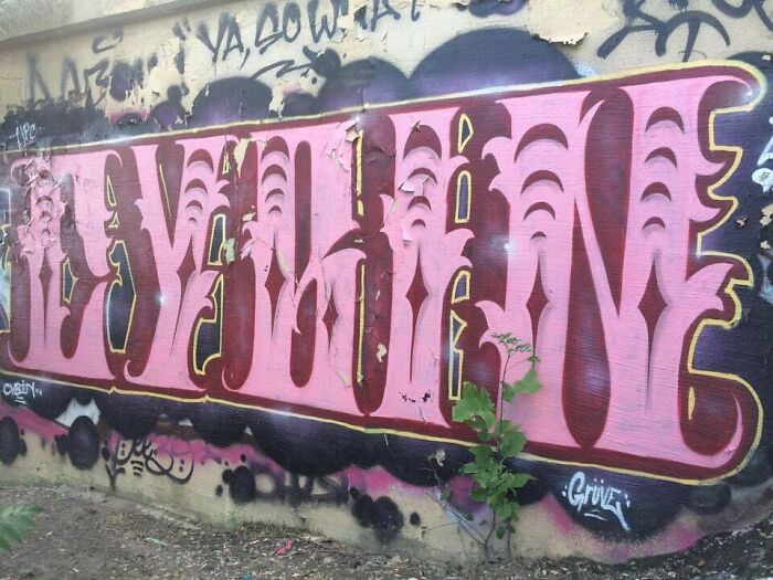 Large pink and maroon graffiti art on a weathered wall, showcasing creative graffiti art that transforms blank walls.