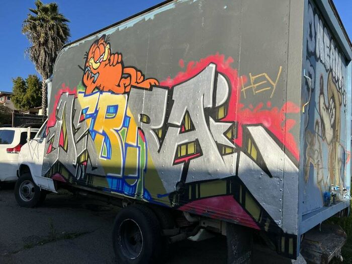 Graffiti art featuring colorful lettering and a cartoon character on the side of a delivery truck in an outdoor setting.