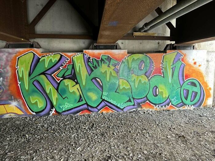 Colorful graffiti art on a concrete wall under a bridge, showcasing creative street art and urban expression.