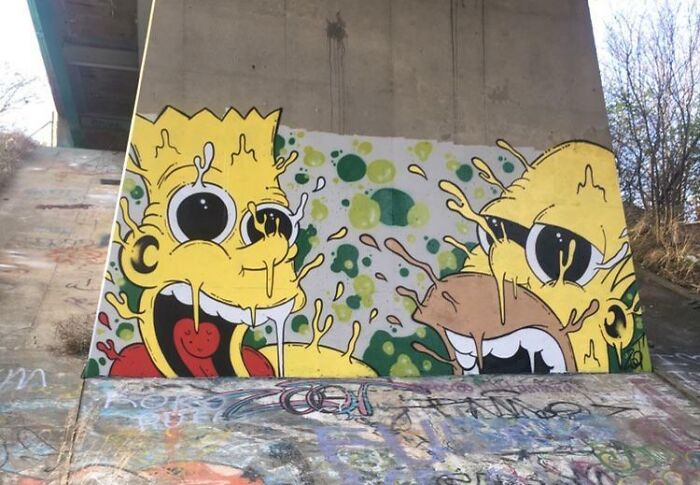 Colorful creative graffiti art of cartoonish faces on a concrete wall under a bridge, showcasing street art admiration.