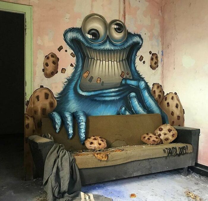 Creative graffiti art on wall featuring a blue cartoon character with cookies transforming a blank space into vivid artwork.
