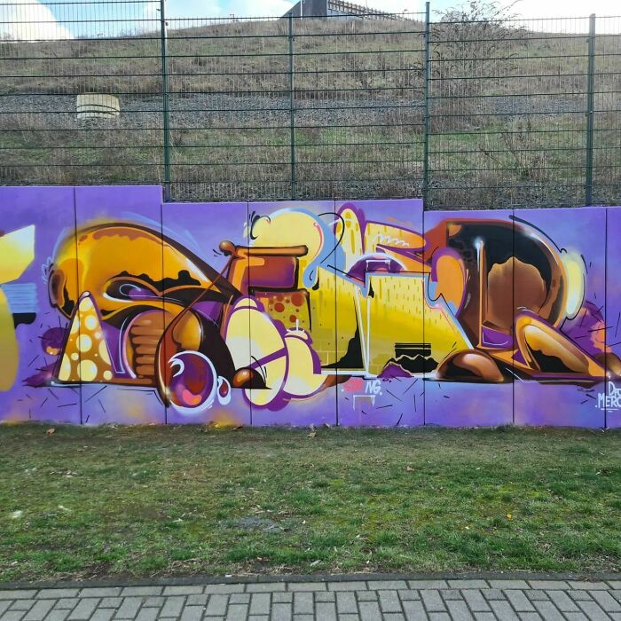 Colorful creative graffiti art on a blank wall featuring abstract shapes and bold yellows blending with purple background.