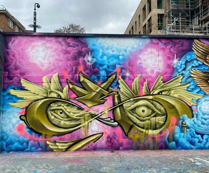 Colorful creative graffiti art on an urban wall featuring abstract golden eyes and vibrant pink and blue background.