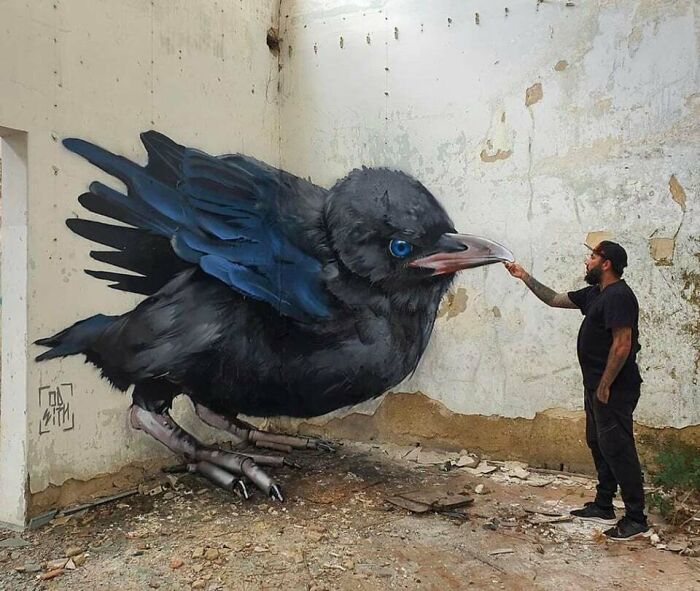 Artist interacting with a large black bird graffiti on a c*****d wall, showcasing creative graffiti art transforming blank walls.
