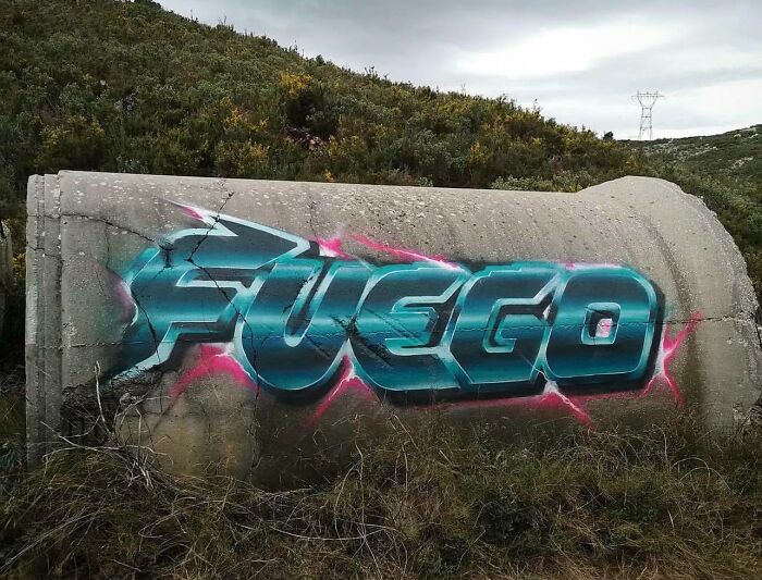 Graffiti art spelling FUEGO in bold blue letters with pink highlights on a c*****d cement wall outdoors.