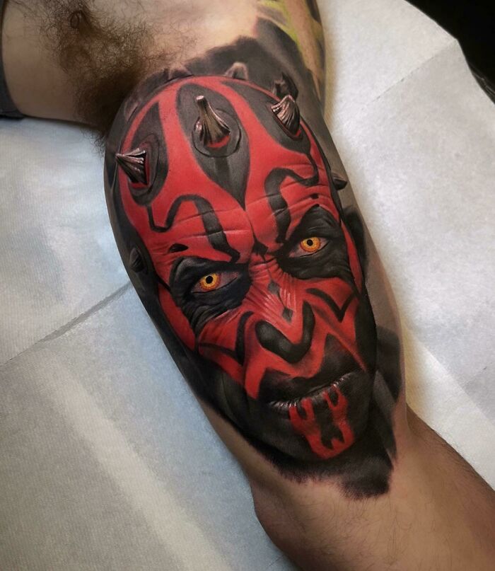 Super realistic tattoo of a red and black horned character, highly detailed on a person's leg.