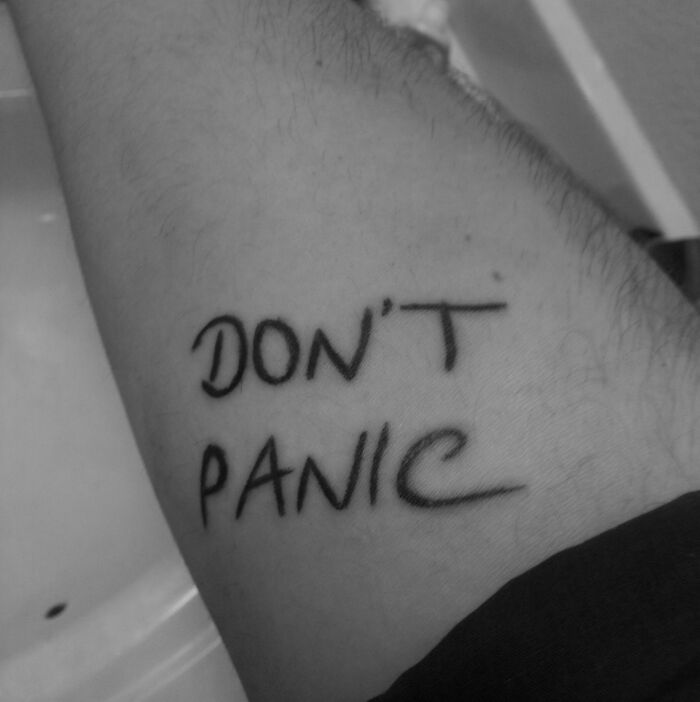 Tattoo on arm reading "Don't Panic" in black ink.