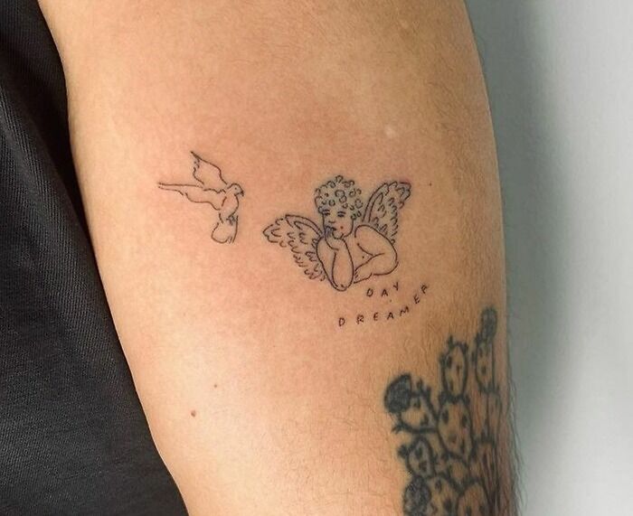 Angel and dove word tattoo on arm with "Day Dreamer" text.
