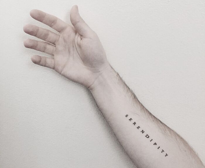 Arm with "serendipity" tattoo in black ink, showcasing a minimalist word tattoo design.