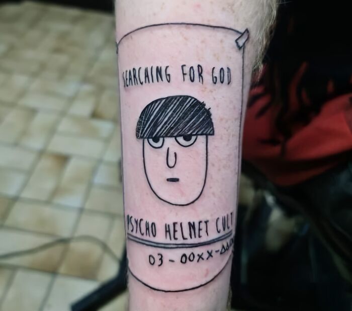 Tattoo of cartoon face with text "Searching for God" and "Psycho Helmet Cult," embodying unique word tattoo design.