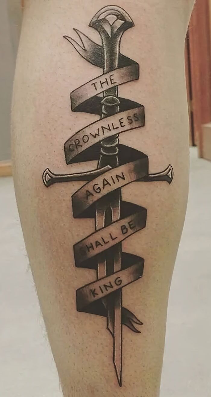 Sword tattoo with ribbon text, "The crownless again shall be king," embodying word tattoos theme.