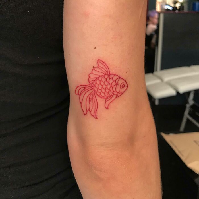 Red ink tattoo of a goldfish on an arm, showcasing unique tattoo design ideas.