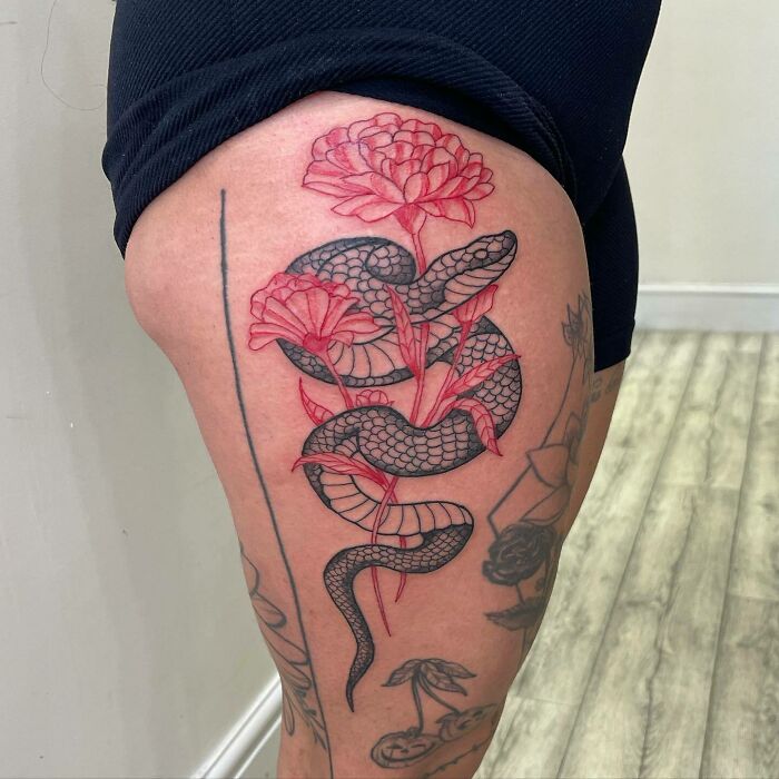 Red ink tattoo design featuring a snake intertwined with flowers on a person's thigh.