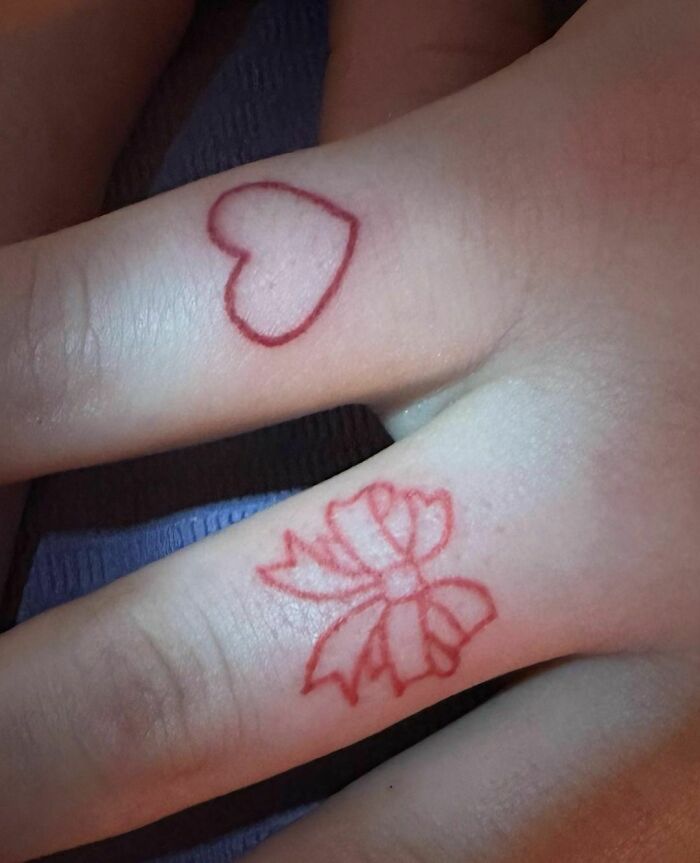 Red ink tattoo designs of a heart and bow on fingers.