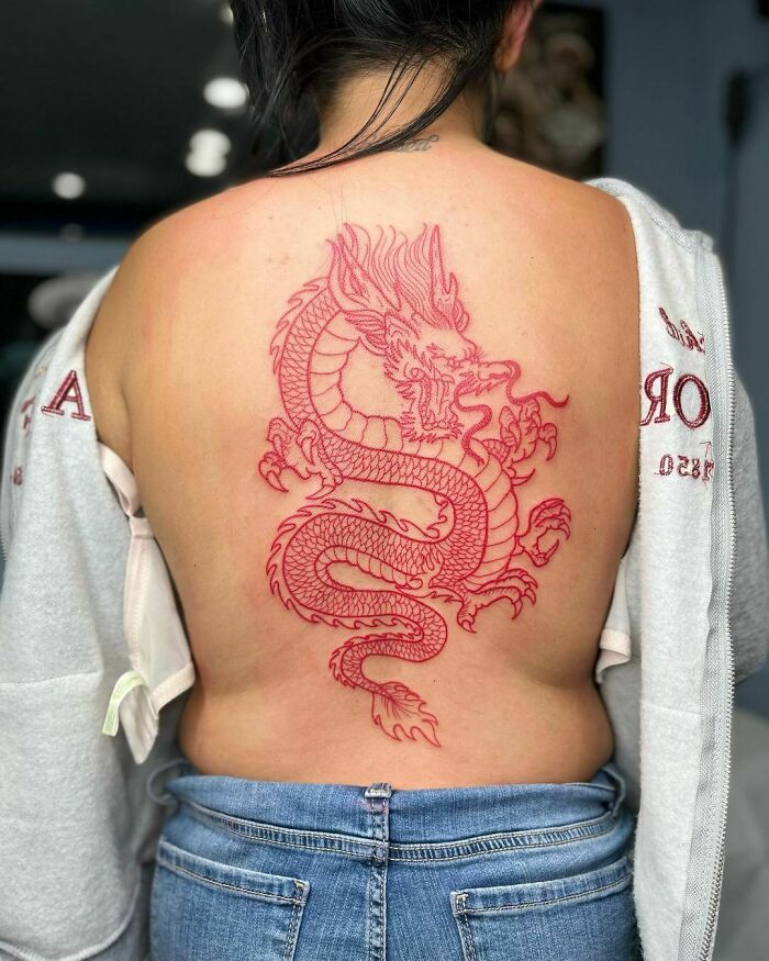Red dragon tattoo design on woman's back, showcasing intricate red ink art, with a casual outfit partially covering the tattoo.