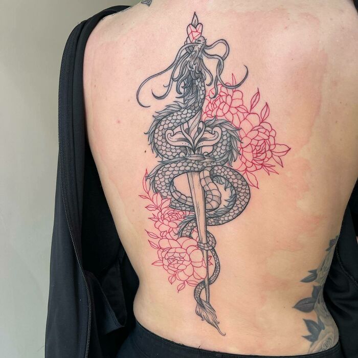 Red ink tattoo featuring an intricate dragon and floral design on a person's back.