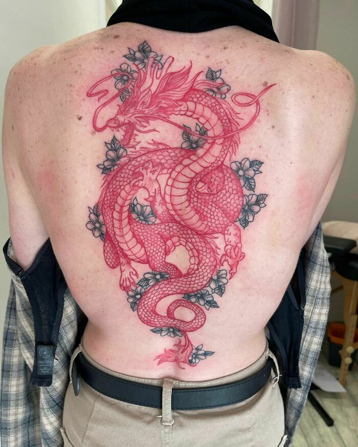 Red ink tattoo design featuring an intricate dragon with floral accents on a person's back.