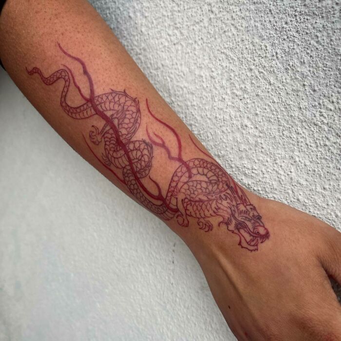 Red ink tattoo of a detailed dragon design on an arm, showcasing intricate artistry in red tattoo ideas.
