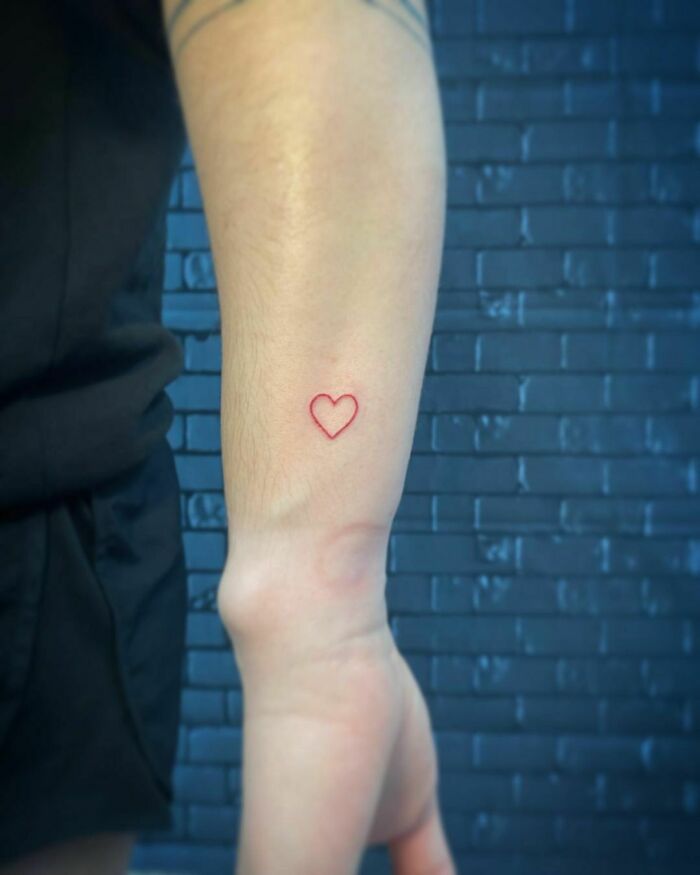 Minimalistic red heart tattoo on forearm, showcasing red ink tattoo design.