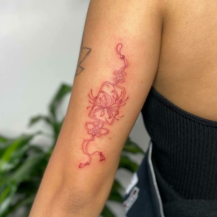Intricate red ink tattoo design on a person's upper arm, featuring floral and abstract elements.