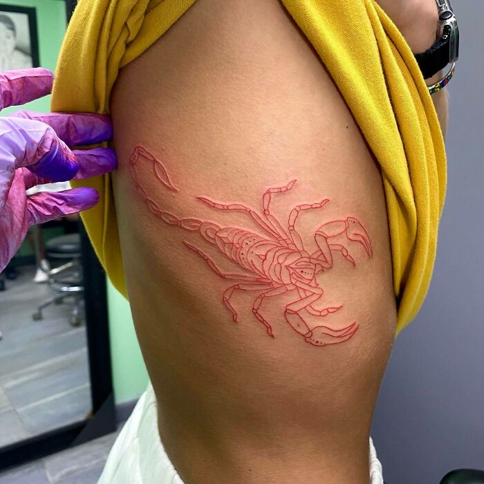 Red ink tattoo of a scorpion on an arm, with intricate detailing, showcased in a tattoo studio.