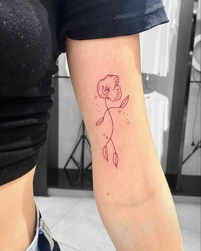Minimalist red ink tattoo of a flower on an arm.