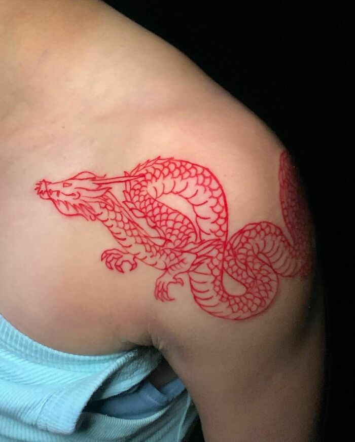 Red ink tattoo of a dragon on a person's shoulder, showcasing intricate design and bold color.