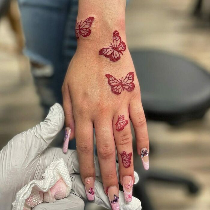 Red ink tattoo of butterflies on a person's hand, showcasing unique tattoo design ideas.