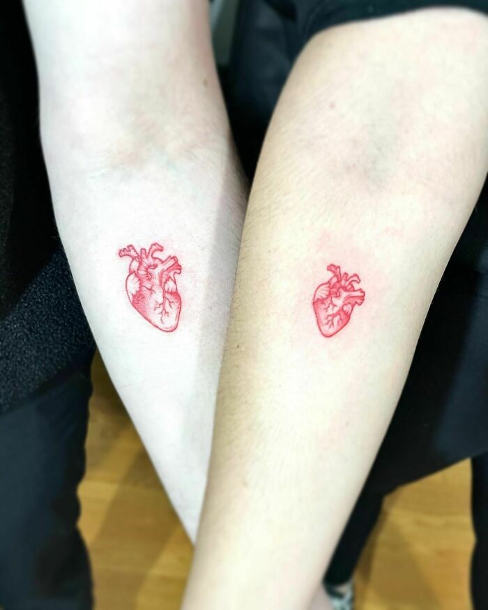 Two forearm tattoos of red ink anatomical hearts, showcasing minimalist red tattoo design.