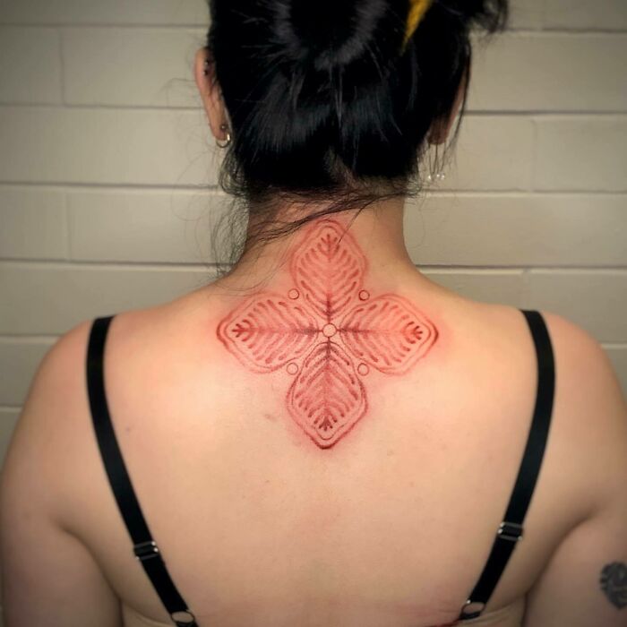 Red ink tattoo design on back in geometric floral pattern.